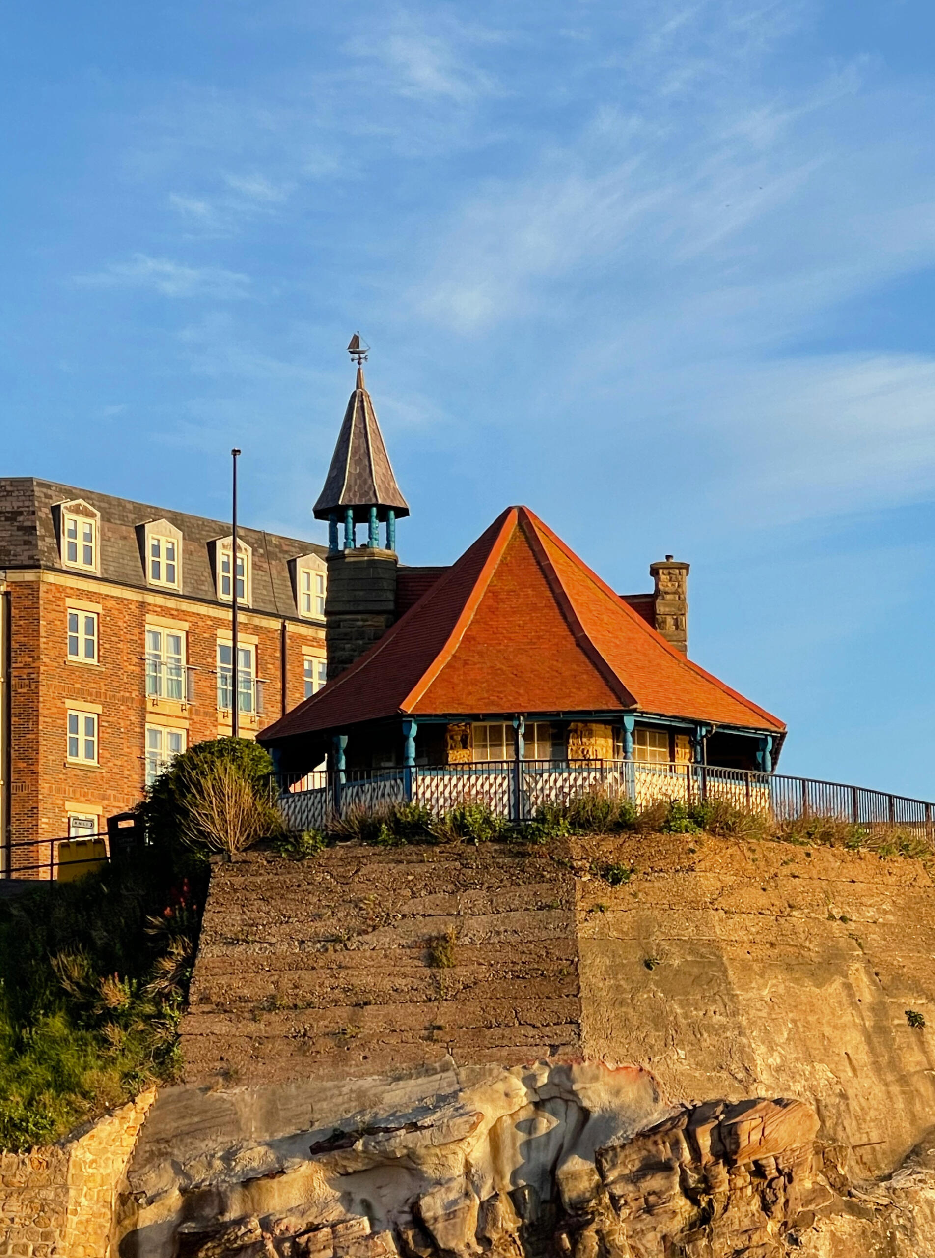A photo of the Watch House from below on the beach, the sun is setting in the background.